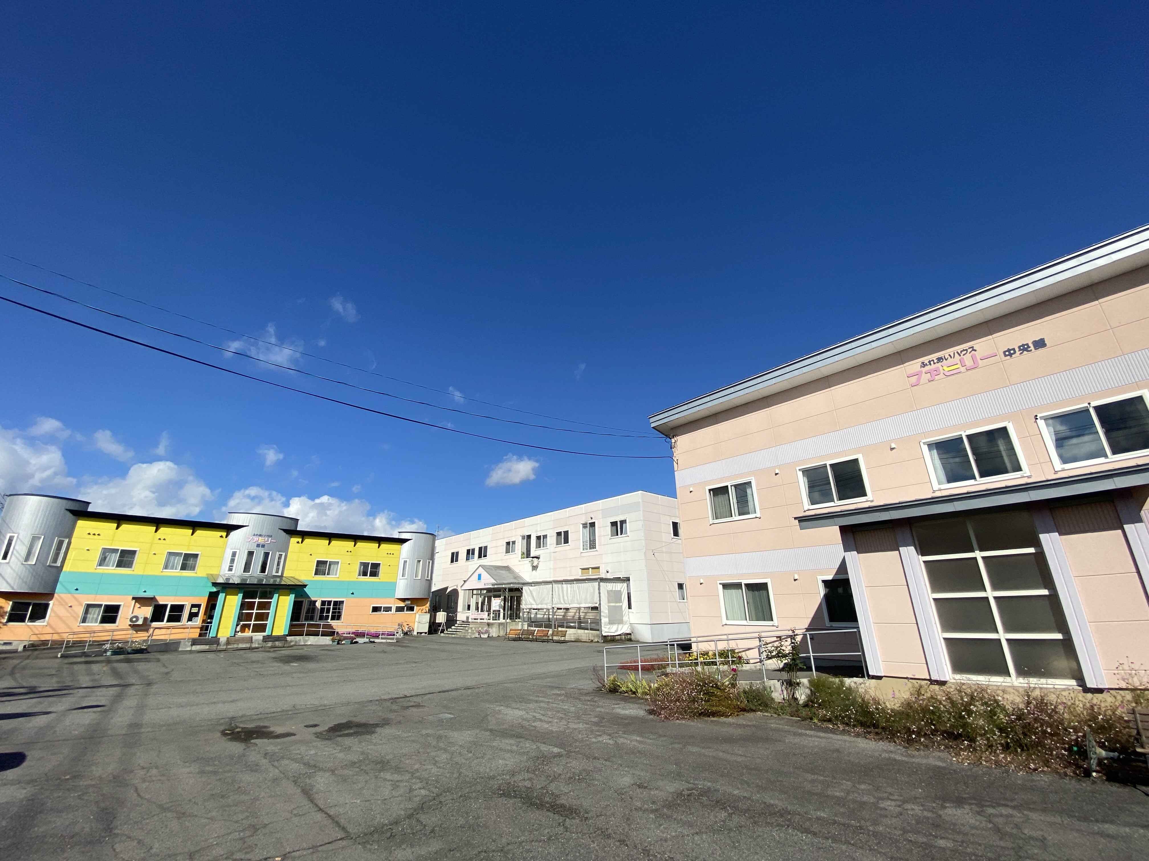 介護施設の外観。黄色と白のツートンカラーの建物が青空の下に立つ